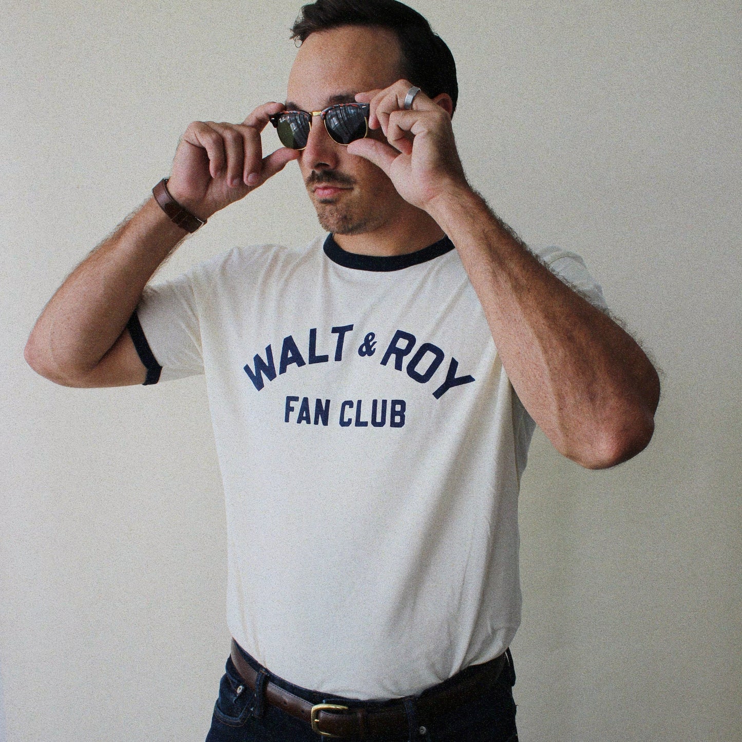 Man wearing a 'Walt & Roy Fan Club' t-shirt, holding sunglasses up to his eyes.