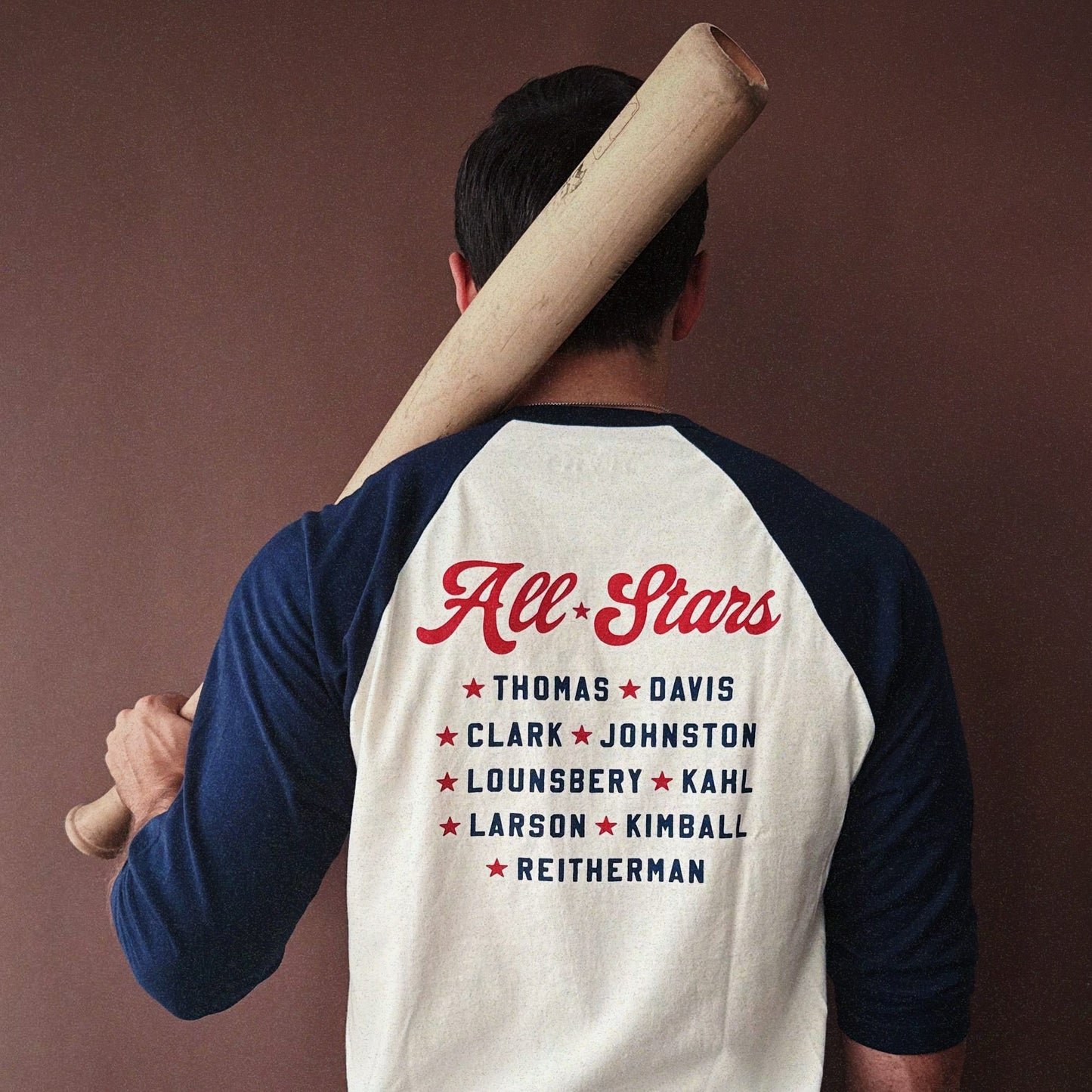 Person wearing the Nine Old Men baseball t-shirt with a bat on a brown background