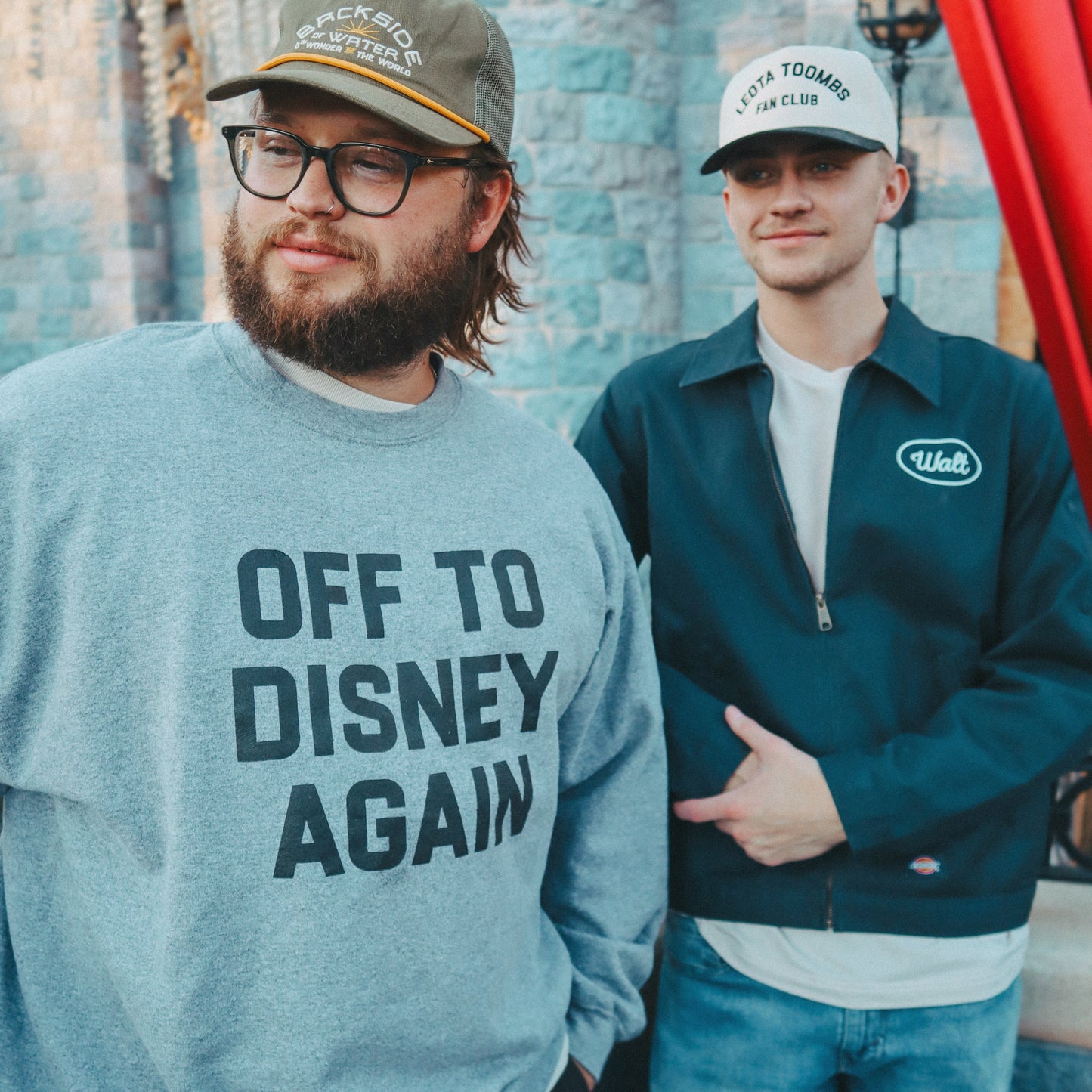 Two people standing in front of a castle with one wearing a 'Off to Disney Again' sweatshirt.