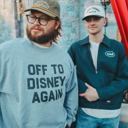 Two people standing in front of a castle with one wearing a 'Off to Disney Again' sweatshirt.