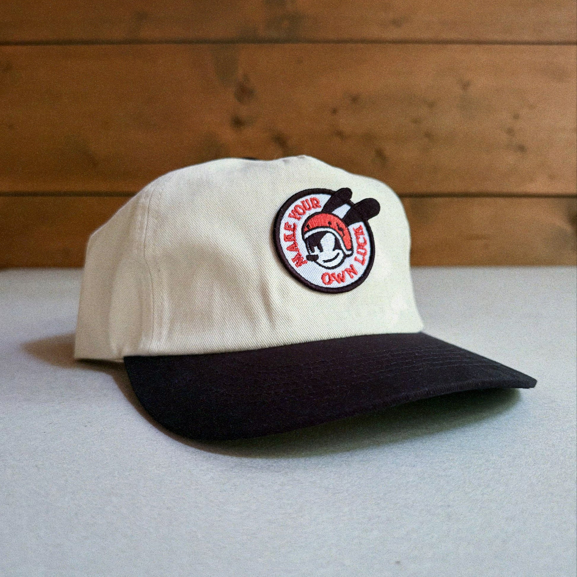 Two-tone natural and black cap with an embroidered patch featuring Oswald The Lucky Rabbit and the phrase 'Make Your Own Luck'