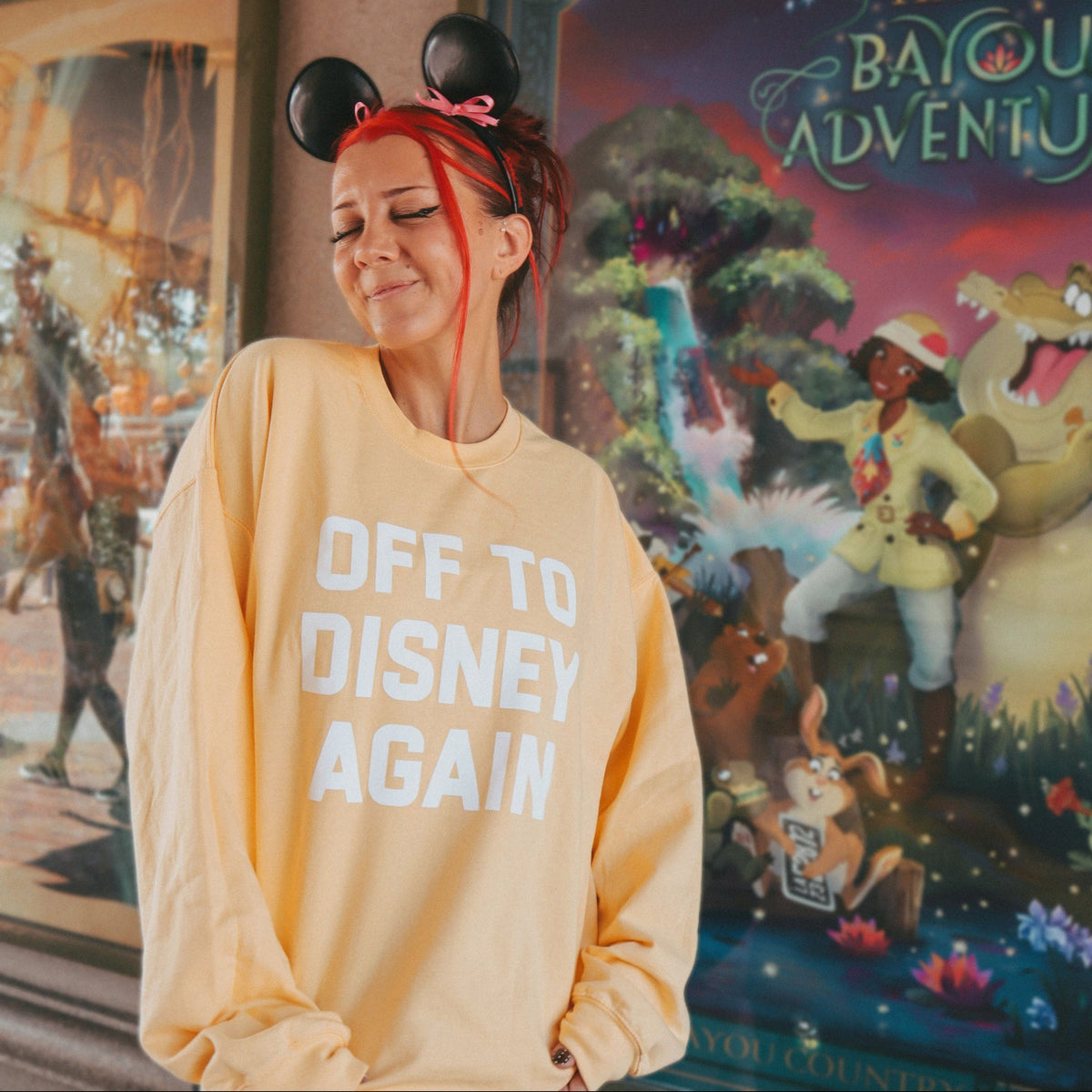 A woman wearing a butter yellow sweatshirt with 'OFF TO DISNEY AGAIN' printed in white
